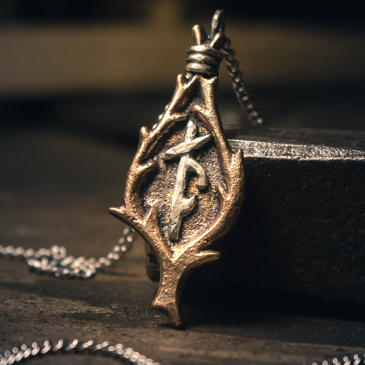 Handforged bronze Norse bindrune pendant with intricate runic symbols, featuring a teardrop-shaped design against a dark textured background