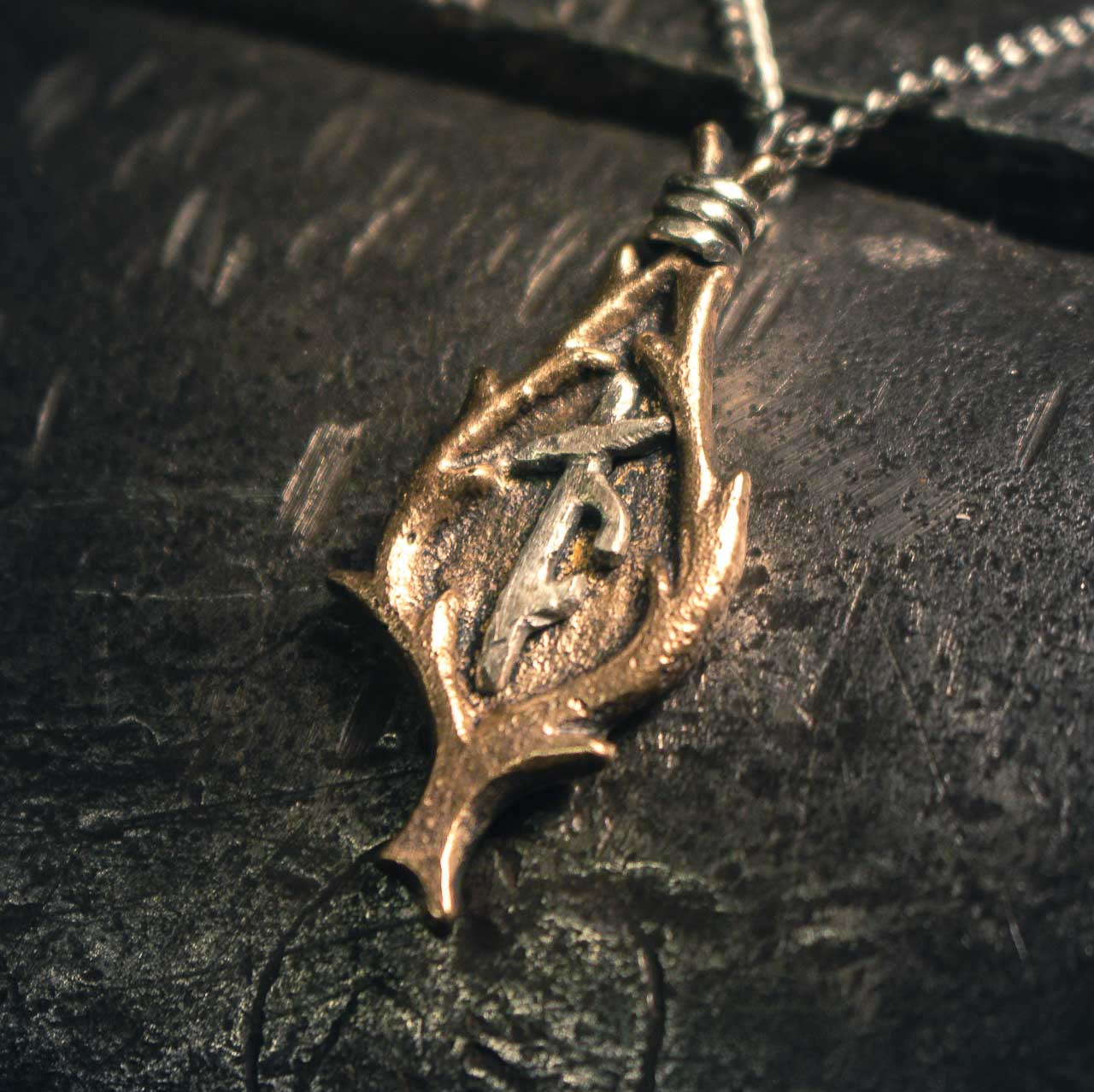Detailed bronze amulet with intertwined runic symbols, photographed with shallow depth of field highlighting the metalwork