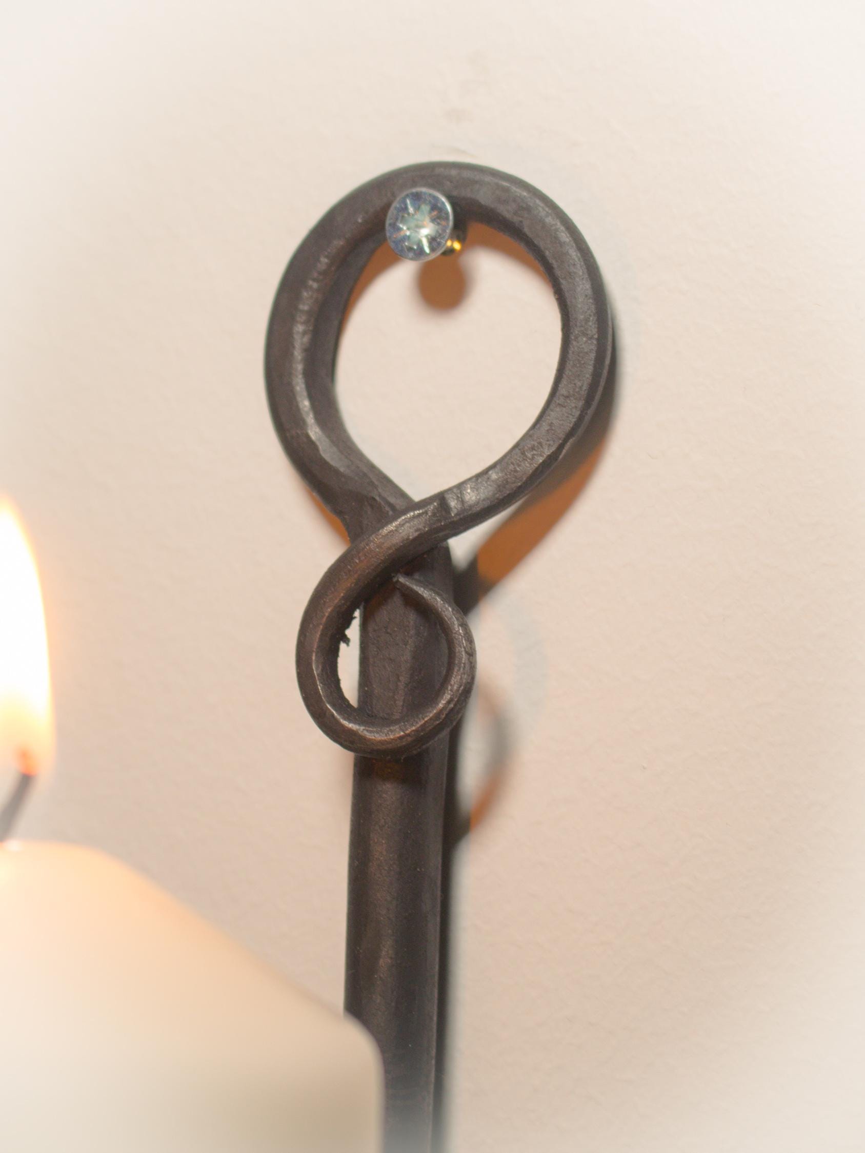 Rustic wall candle sconce crafted from hand-forged iron, holding a lit candle.