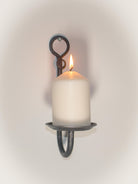 Rustic iron wall sconce holding a white candle, perfect for home decor.