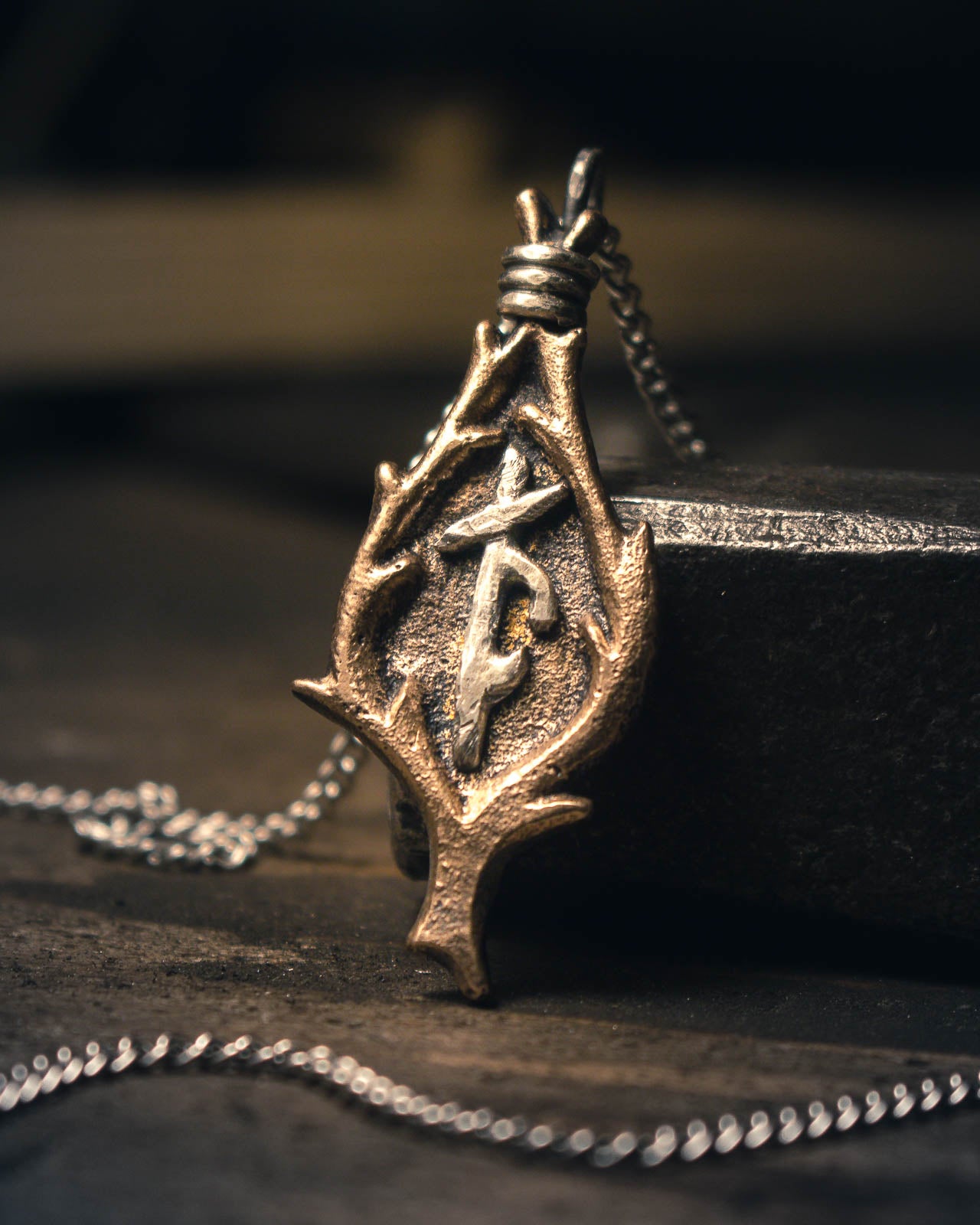 Handforged bronze Norse bindrune pendant with intricate runic symbols, featuring a teardrop-shaped design against a dark textured background